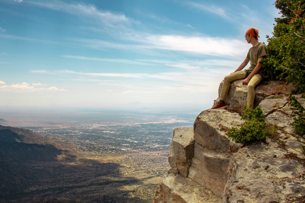 Man sitting on the edge and enjoying the vistas from one of the many Albuquerque hiking trails in the Sandia Mountains